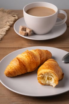 Freshly baked croissants served with a hot cup of coffee on a wooden table in a cozy setting.