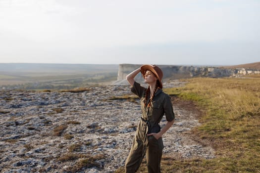 Woman in hat standing on top of hill overlooking valley in background during travel adventure on fashionable trip
