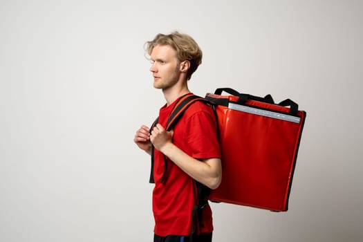 Profile view of delivery man in red shirt and thermal backpack. Represents fast service, urban logistics and gig economy lifestyle.