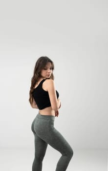 Slim woman in black top and leggings posing on white background. Fitness model, healthy lifestyle concept.