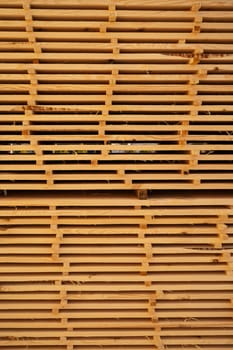 Close-up view of stacked kiln-dried lumber planks arranged in a tight grid. The photo shows details of processed wood texture with sawdust and separators, ideal for construction themes.