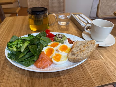Healthy breakfast plate with vegetables, eggs and salmon served with herbal tea. Balanced nutrition and clean eating in a modern cafe.