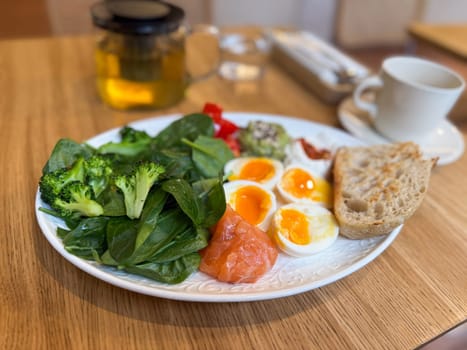 Healthy breakfast plate with vegetables, eggs and salmon served with herbal tea. Balanced nutrition and clean eating in a modern cafe.