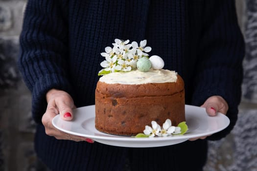 A woman holding a plate with a homemade Easter cake decorated with spring flowers and eggs. Horizontal.