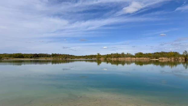 Tranquil lake landscape with clear water reflecting blue sky and lush greenery, serene nature scene ideal for relaxation and meditation, peaceful outdoor escape, nature concept, creating a serene nature scene perfect for relaxation and meditation, an ideal outdoor escape