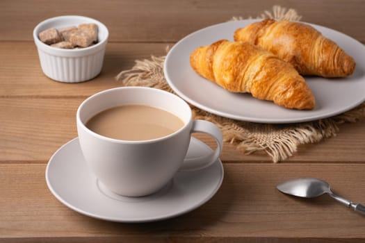 Freshly baked croissants served with a hot cup of coffee on a wooden table in a cozy setting.