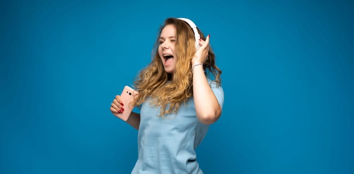 Smiling girl with headphones dancing and listening to music while holding a phone.