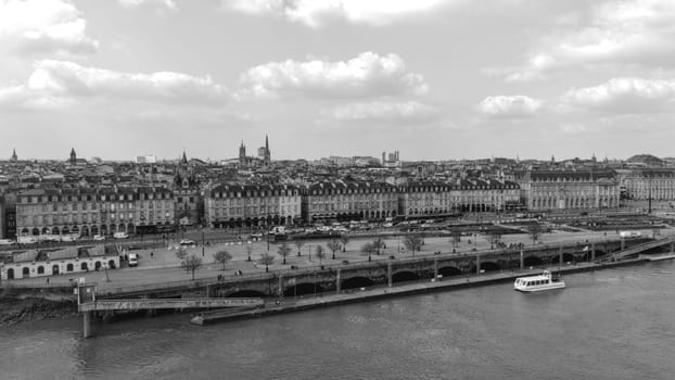 Monochrome view of Bordeaux, France, showing classical architecture along the Garonne River with a sightseeing boat in foreground.