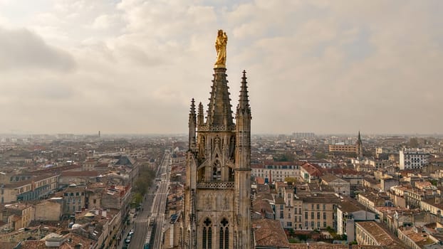 Close up view of the Pey Berland Tower in Bordeaux France with golden statue and panoramic cityscape under cloudy sky