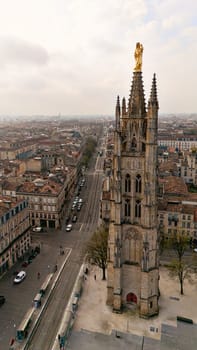 Close up view of the Pey Berland Tower in Bordeaux France with golden statue and panoramic cityscape under cloudy sky