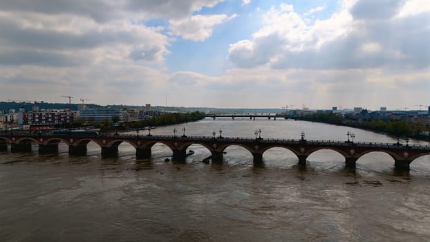 Historic Pont de Pierre spans the Garonne River in Bordeaux, France, with dramatic skies and cityscape in the background.