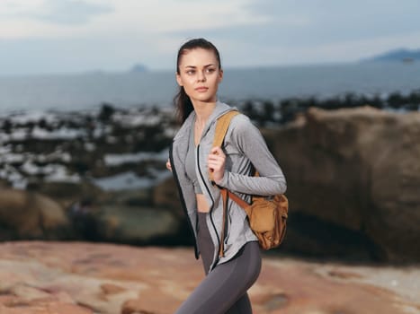 Confident female model in athletic clothing against a rocky coastal backdrop, perfect for promoting fitness, adventure, and healthy lifestyles