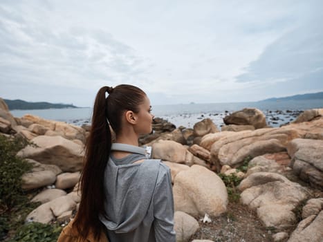 A young woman in activewear stands on a rocky shore, gazing at the ocean and contemplating nature The image promotes healthy lifestyle, mindfulness, and appreciation for natural beauty