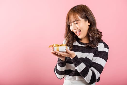 Portrait of happy beautiful Asian young woman smiling holding small gift box on hands, studio shot isolated on pink background, gift for you. Birthday, New year, Christmas, valentine day concept
