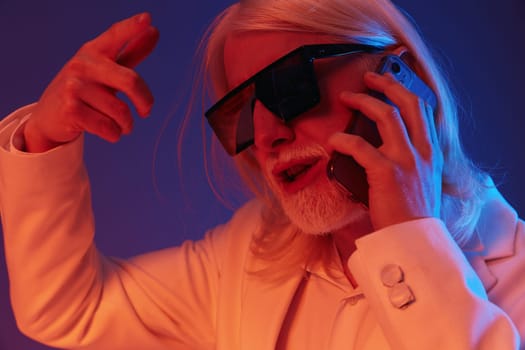 A fashionable older man with long white hair and sunglasses is engaged in a lively phone conversation The background features striking blue and purple hues, adding to the trendy and energetic vibe of the image