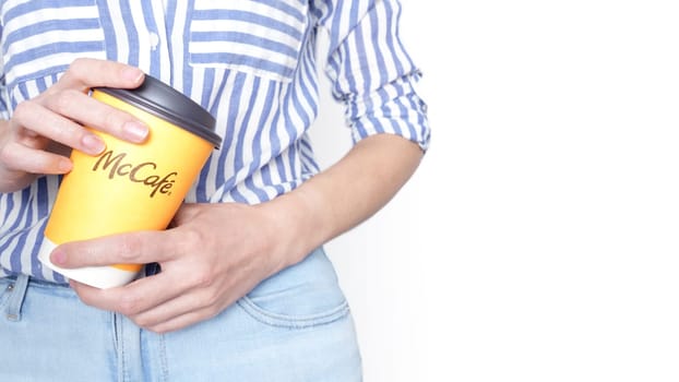 Woman holding a yellow McCafe coffee cup wearing blue jeans and blue striped shirt. Ottawa ON Canada 06-17-2024.