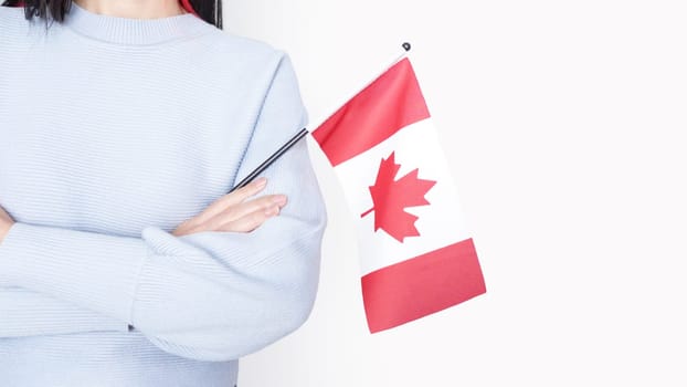 Unrecognized girl student in blue shirt holding small Canadian flag over gray background, Canada day, holiday, vote, immigration, tax, copy space.