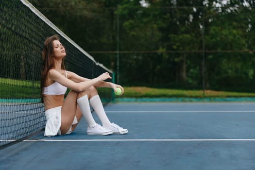 A young athletic female, dressed in a sporty tennis outfit with a skirt and top, relaxes on a tennis court, surrounded by greenery, embodying balance and leisure in sports