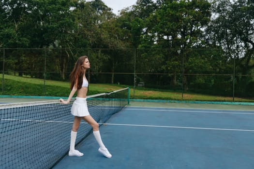 Confident young female tennis player in sporty attire stands on a vibrant tennis court, surrounded by lush greenery, embodying energy and determination in a dynamic sports concept