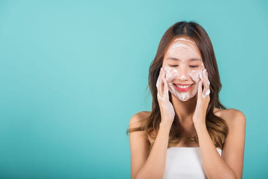 Asian woman face wash exfoliate scrub soap foam with skincare cleansing, Portrait beautiful female smile applies foaming cleanser healthy skin, Studio isolated on blue background, beauty skincare