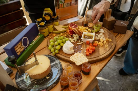 Tasting cheese and fruit platter at a farmers market. Close-up of a woman's hand tasting cheese and sauce with a wooden stick. Large assortment of natural products on the table