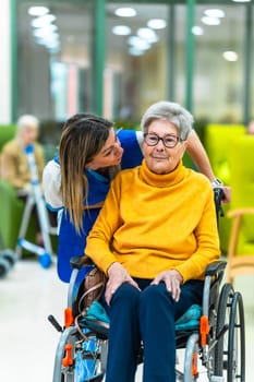 Nurse supporting and comforting elderly woman sitting in wheelchair in retirement home, providing care and companionship