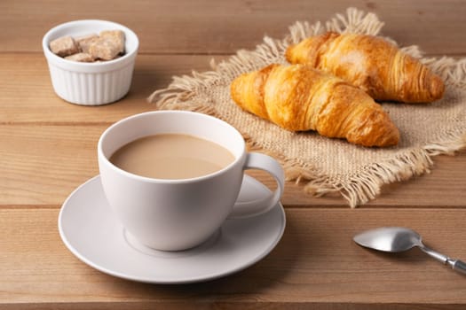 Freshly baked croissants served with a hot cup of coffee on a wooden table in a cozy setting.