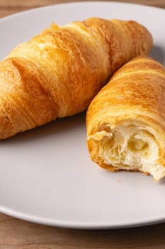 Two freshly baked croissants rest on a simple plate, displaying their flaky texture and golden brown color. The cozy kitchen setting highlights the deliciousness of this pastry.