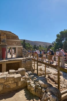 Crete.Greece - april 26, 2025: Iconic architectural marvels of Knossos reflecting the grandeur of the Minoan civilization with detailed stone ruins and vivid red pillars in an open historical site.