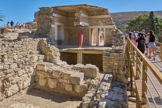 Crete.Greece - april 26, 2025: Stunning view of the ancient ruins of Knossos with red columns standing tall amidst historical stone architecture and cultural heritage under clear blue skies.