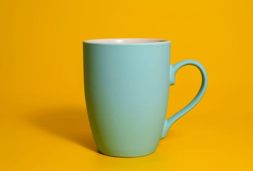 A single matte blue ceramic mug with a handle is placed against a solid yellow backdrop, minimal and clean studio lighting.