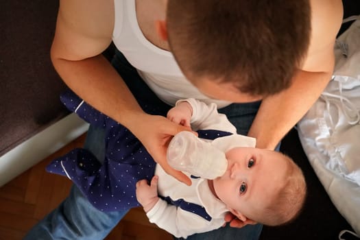 Young man feeding milk his baby boy son from bottle, view from above