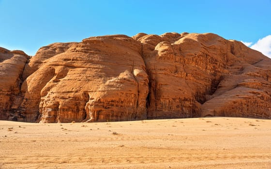 Rocky massifs on red sand desert, bright blue sky in background - typical scenery in Wadi Rum, Jordan
