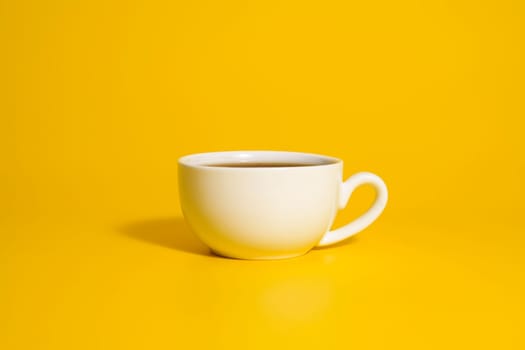 Minimalist white teacup filled with tea placed against a vivid yellow backdrop, creating strong contrast and clean modern design.