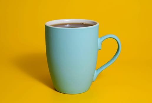 A tall matte blue ceramic mug filled with coffee stands on a vibrant yellow background with soft lighting and a clean minimalist setup.