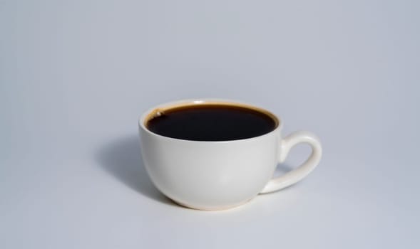 A simple white cup filled with black coffee placed against a clean light background, casting a soft shadow.