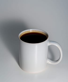 A white ceramic mug filled with black coffee, placed on a smooth light surface with a soft shadow, captured in a minimal and clean composition.