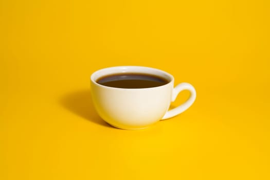 Minimalistic white cup of black coffee placed on a vibrant yellow backdrop, creating a bold and modern visual.