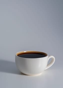 A minimalist white ceramic cup filled with black coffee, placed on a soft gray surface with gentle lighting and subtle shadow.
