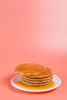 Dutch stroopwafels stacked on a white plate with warm melted caramel oozing out, set against a soft pink background.