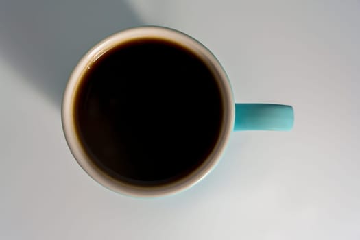 A flat lay of a filled turquoise coffee mug on a light background, with strong shadow and minimalistic composition.
