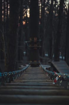 A close-up view of a wooden rope bridge leading to a tree platform in a forest adventure park, captured during the evening with soft, fading light.