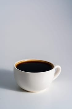 A simple white ceramic cup brimming with black coffee, placed on a clean white surface in soft lighting with minimal shadows.