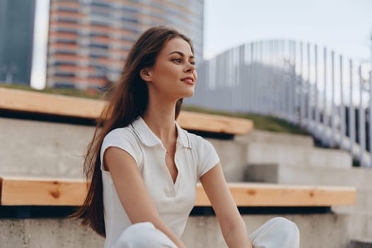 A confident woman in casual business attire sits outdoors, radiating positivity and professionalism in a modern urban environment.