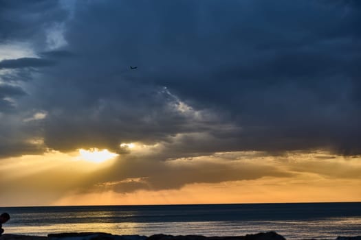 A professional woman in formal wear gazing toward the horizon, embodying ambition against a stunning ocean view at sunset, balancing serenity and strength.