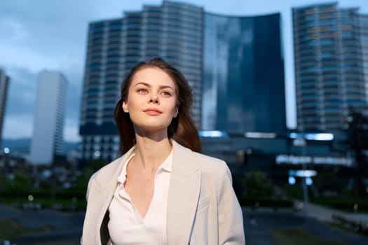 A focused woman in a sophisticated outfit stands confidently against a modern city backdrop, showcasing her determination and ambition in a professional setting.