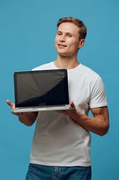 Smiling man presenting open laptop device standing against vibrant blue studio background. Focused on technology and communication, this portrait captures a cheerful professional in a casual outfit. Concept: digital confidence