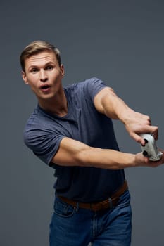 focused young man playing video game holding joystick wearing casual blue t-shirt and jeans with intense facial expression isolated on plain gray background studio portrait digital entertainment concept