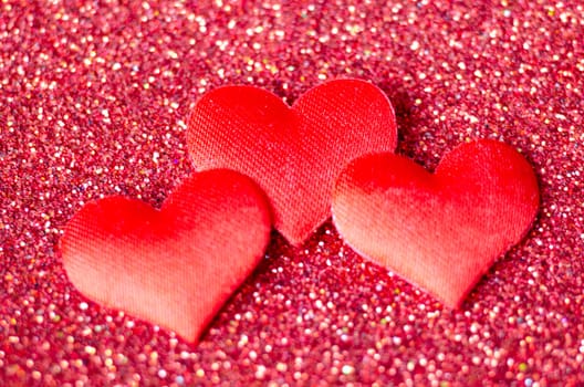 Top view of 3 tiny red hearts on sparkle red background with customizable space for text or wishes.