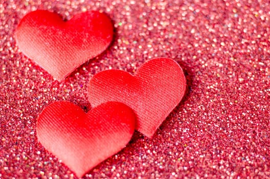 Top view of 3 tiny red hearts on sparkle red background with customizable space for text or wishes